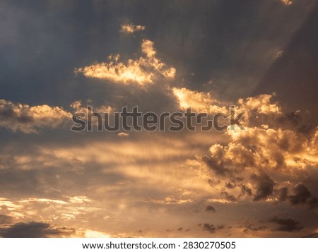 Sunlight breaks through clouds at sunset. Golden rays illuminate scattered cumulus clouds. Sky shows warm orange and dark blue tones