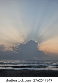 Sunlight breaks through thick clouds over the ocean, casting soft rays across the calm waves.