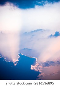 Sunlight bursts through dramatic blue and purple clouds, casting ethereal rays across a sky filled with soft pink and white hues. This atmospheric scene captures a moment of beauty and light breaking through darkness.
