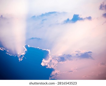Sunlight bursts through dramatic blue and purple clouds, casting ethereal rays across a sky filled with soft pink and white hues. This atmospheric scene captures a moment of beauty and light breaking through darkness.