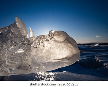 Sunlight bursts through a jagged, translucent ice boulder washed up on the shore of Otsu Coast, Hokkaido, against a deep blue winter sky.