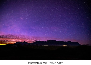 Sunlight And Car Lights Below Night Sky And Chisos Mountain Range In Big Bend National Park