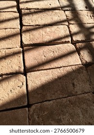 Sunlight casts soft linear shadows across textured brick pavement, creating a warm abstract pattern with natural tones, depth, and minimalist outdoor composition.