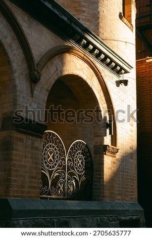 Sunlight casts soft shadows on the ornate metal gates and brick wall of a building during golden hour in the evening.