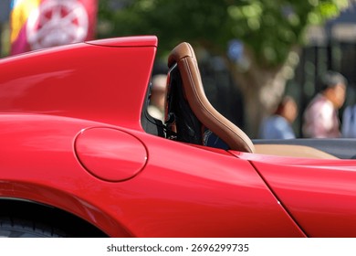 Sunlight creates alluring shadows on sports car's tan leather seat. White precision stitching runs up backrest's curved contour, flowing with smooth elegant line of the convertible's red body.