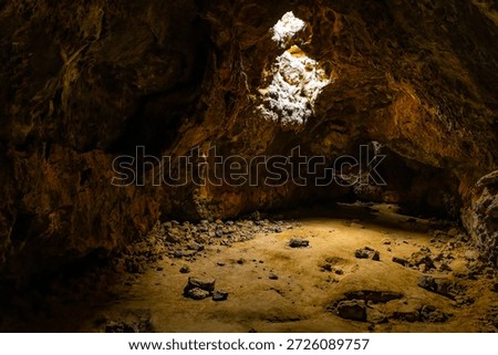 Sunlight enters through ceiling openings illuminating the interior of a lava tube cave in the Mojave Desert