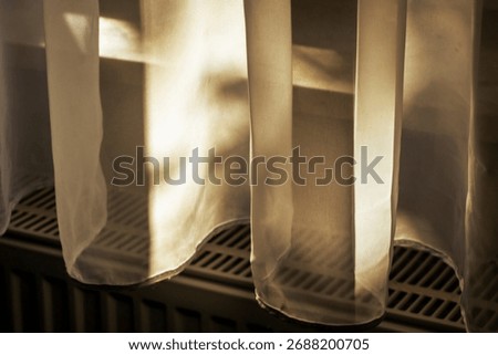 Sunlight filtering through sheer white curtains, creating a soft and warm atmosphere. The light reflects off a radiator below, adding a cozy touch to the interior space.