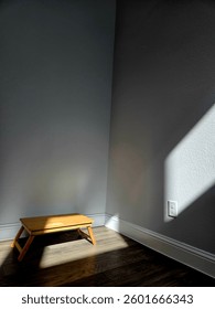 Sunlight gently streams through the window, casting a warm glow on the wooden table, while the rest of the room lingers in quiet darkness — capturing a sense of stillness and solitude.