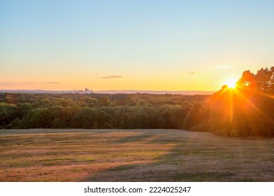 Sunlight at golden hour on grassy field with shadows and skyline in distance - Powered by Shutterstock