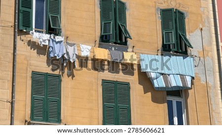 Sunlight hits laundry drying on a line outside a yellow Italian building with shutters