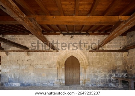 Sunlight illuminates the textures of aged stone walls and rustic wooden beams, creating a captivating scene of historical architecture with an arched doorway