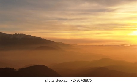 Sunlight illuminating distant mountains and rolling hills covered in mist during golden hour