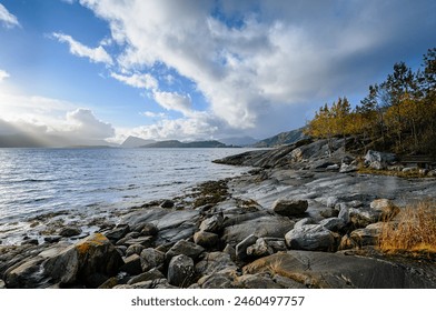 Sunlight kisses the rocky shore under a dramatic sky, by the tranquil sea, as the day winds down. - Powered by Shutterstock