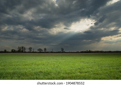 Sunlight passing through a hole in the clouds onto a green meadow, spring landscape