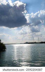 Sunlight peeks through clouds over a tranquil lake, creating a sparkling reflection on the water.