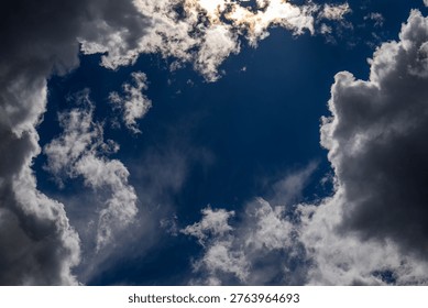 Sunlight pierces through dramatic, fluffy white clouds against a deep blue sky