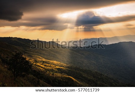 The sunlight rays make their way through the clouds in the mountains