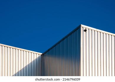 Sunlight reflection on surface of corrugated steel wall of industrial building against blue clear sky background in low angle view