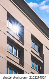Sunlight reflection on surface of multiple blue glass windows on gray office building wall against white cloud and blue sky in vertical frame