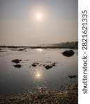 Sunlight reflection over shallow tidal pools and rocks at low tide beach during golden hour