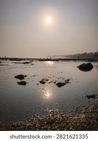 Sunlight reflection over shallow tidal pools and rocks at low tide beach during golden hour