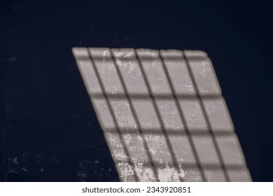 sunlight and shade pattern on old grey wall in dark jail. Prison, jail or basement theme.
