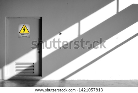 Sunlight and shadow on surface of gray wall and door of electrical control room with yellow warning sign in minimal style, exterior architecture concept 