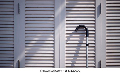 Sunlight and shadow on surface of the old metal walking stick on white wooden folding wall background 