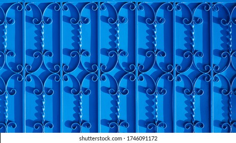 Sunlight and shadow on surface of wrought-iron elements pattern on vintage blue metal gate door background, exterior architecture concept