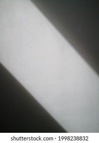 The sunlight shines in diagonal lines on the white plaster wall, creating dark shadows on both sides.