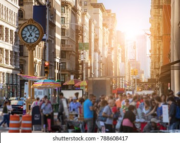 Sunlight Shines On The Buildings Of Manhattan With Crowds Of People Shopping At Street Vendors In New York City