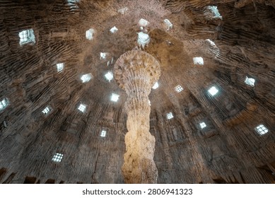 Sunlight shines through small windows into a unique man-made cave featuring a large stone pillar built over a footprint of Buddha at Wat Klai Kangwon in Chai Nat, Thailand.