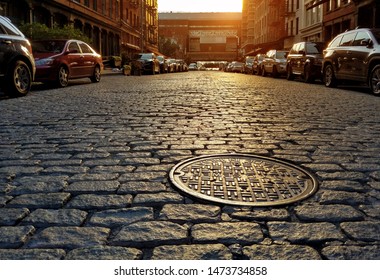 Sunlight shining on a cobblestone street and manhole cover in Manhattan New York City NYC