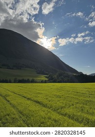 Sunlight shining through clouds above green fields and mountains in the Norwegian countryside