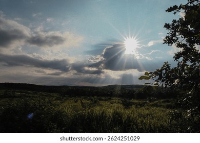 Sunlight shining through clouds over a green rural landscape.