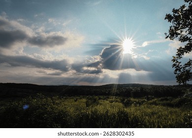 Sunlight shining through clouds over a green rural landscape.