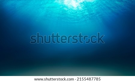 Sunlight shining through the surface of the blue ocean, sea, with dark waters and sandy seabed below.