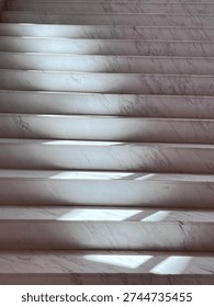 Sunlight shining through a window creating rhythmic shadows on marble stairs. 