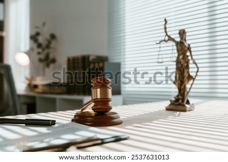 Sunlight streaming through blinds illuminates a judge's gavel and themis statue on a desk in a law office