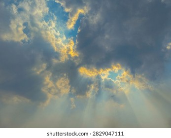 Sunlight streaming through dense clouds creates dramatic rays of light across a soft blue and golden sky.