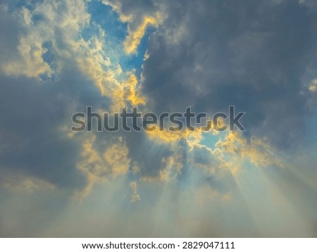 Sunlight streaming through dense clouds creates dramatic rays of light across a soft blue and golden sky.