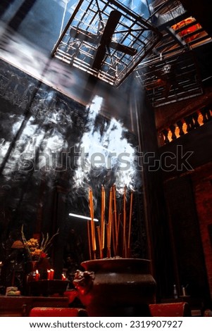 Sunlight streaming through a vent highlighting the smoke from burning incense inside a buddhist temple. Vietnam