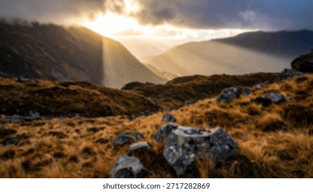 Sunlight streams through clouds over grassy hills and distant mountains, illuminating a rocky landscape.