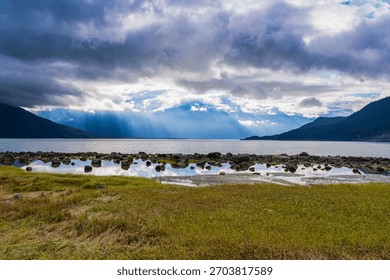 Sunlight streams through dramatic clouds over Kachemak Bay, illuminating distant mountains.