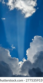 Sunlight streams through towering clouds in a vertical portrait, creating dramatic crepuscular rays that pierce a vibrant blue sky in a divine glow.