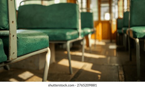 Sunlight streams through the windows, casting shadows on the worn, green upholstery of empty seats inside an old-fashioned tramcar
