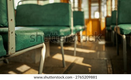 Sunlight streams through the windows, casting shadows on the worn, green upholstery of empty seats inside an old-fashioned tramcar