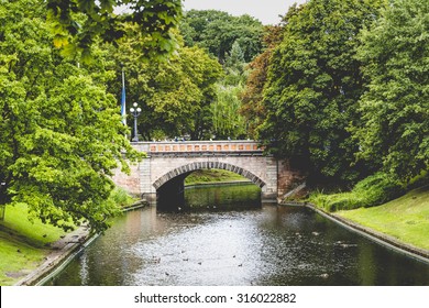 Sunlight Through The Trees In The Park And The Tourist Boat Sailing Under The Bridge Through The Channel. Riga, Latvia