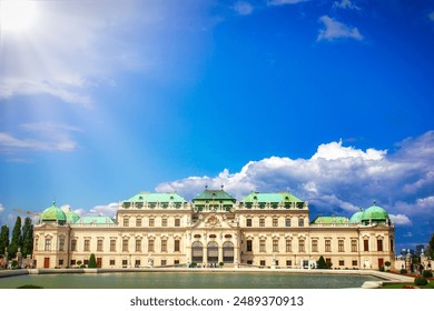 Sunlit Belvedere Palace, Vienna; historic architectural grandeur with reflective pool view. Ornate detailing, tranquil park setting, and vibrant green-domed roofs under a partly cloudy sky. - Powered by Shutterstock