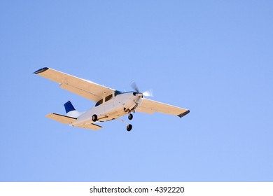 Sunlit Cessna Light Aeroplane Flying In Clear Blue Sky.